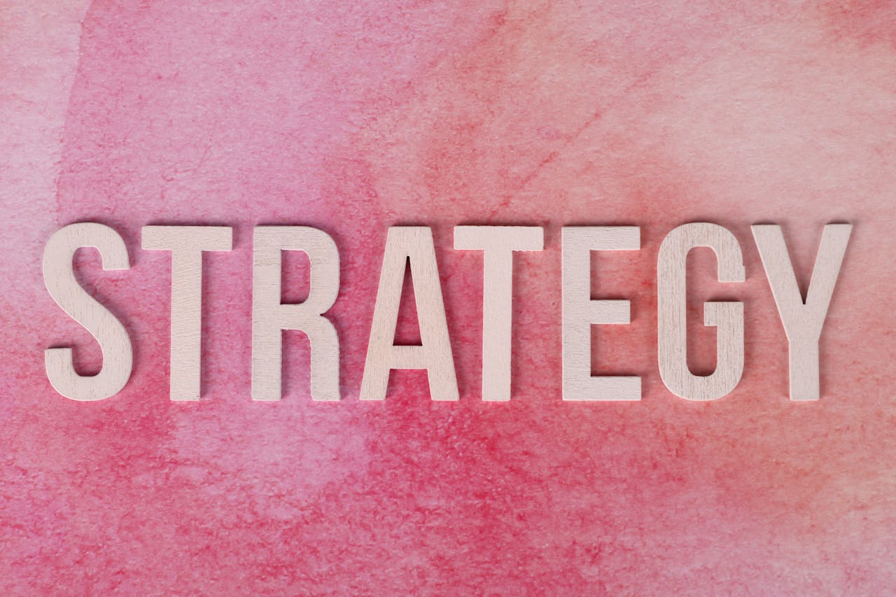 Wooden letters spelling Strategy on a pink textured background.